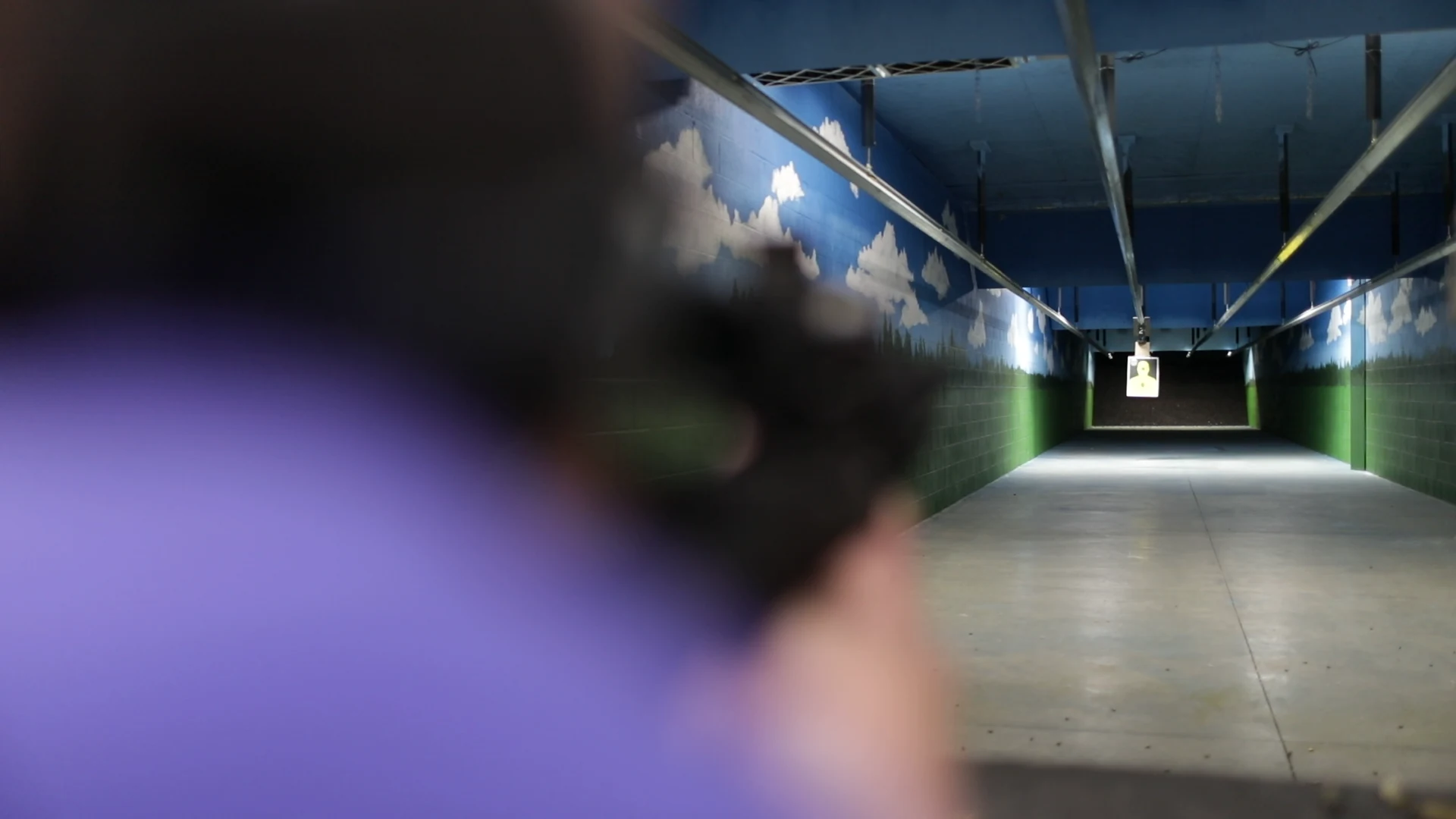 View down the indoor rifle range with a shooter in the foreground.
