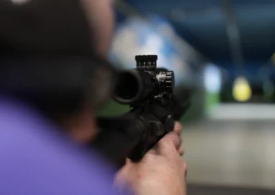 Close view of a shooter aiming a scoped rifle down the indoor range.